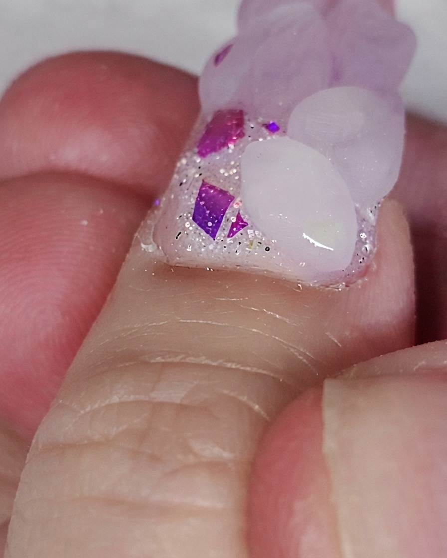 Un pinceau à ongles plaçant une perle dacrylique rose sur une base dongle pailletée pour former un cœur.
