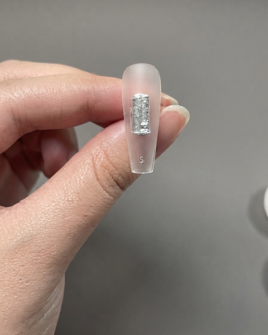 Extension dongle transparente tenue entre les doigts montrant un coup de pinceau appliqué directement sans base coat.