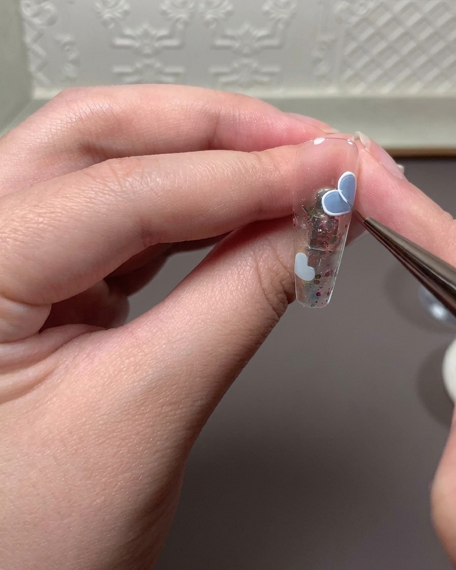 Pinceau fin appliquant un mélange de gel en relief et de gel blanc pour repasser sur le contour dun cœur.