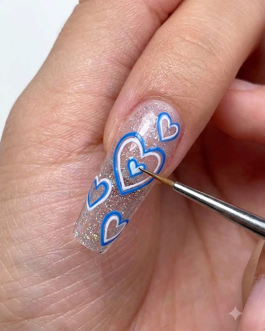 Pinceau de détail utilisant du gel blanc pour dessiner de petits cœurs en 3D sur un ongle long et pailleté.