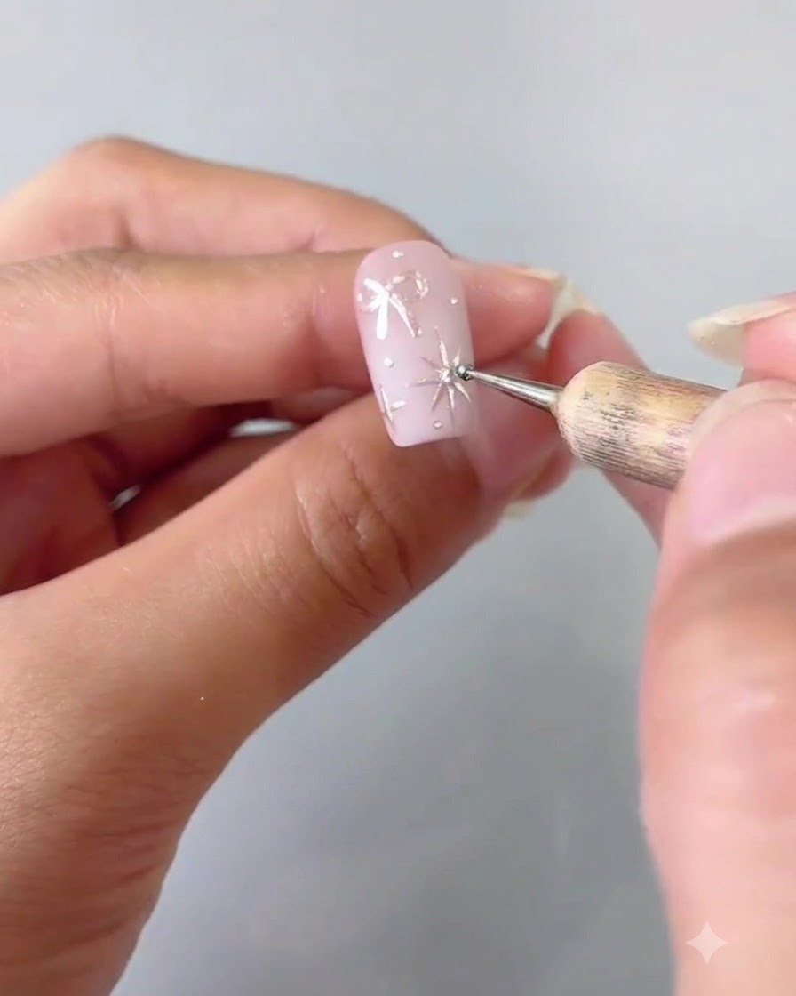Gros plan montrant un outil de dotting plaçant soigneusement un minuscule cristal au centre dune étoile argentée peinte sur un ongle rose.