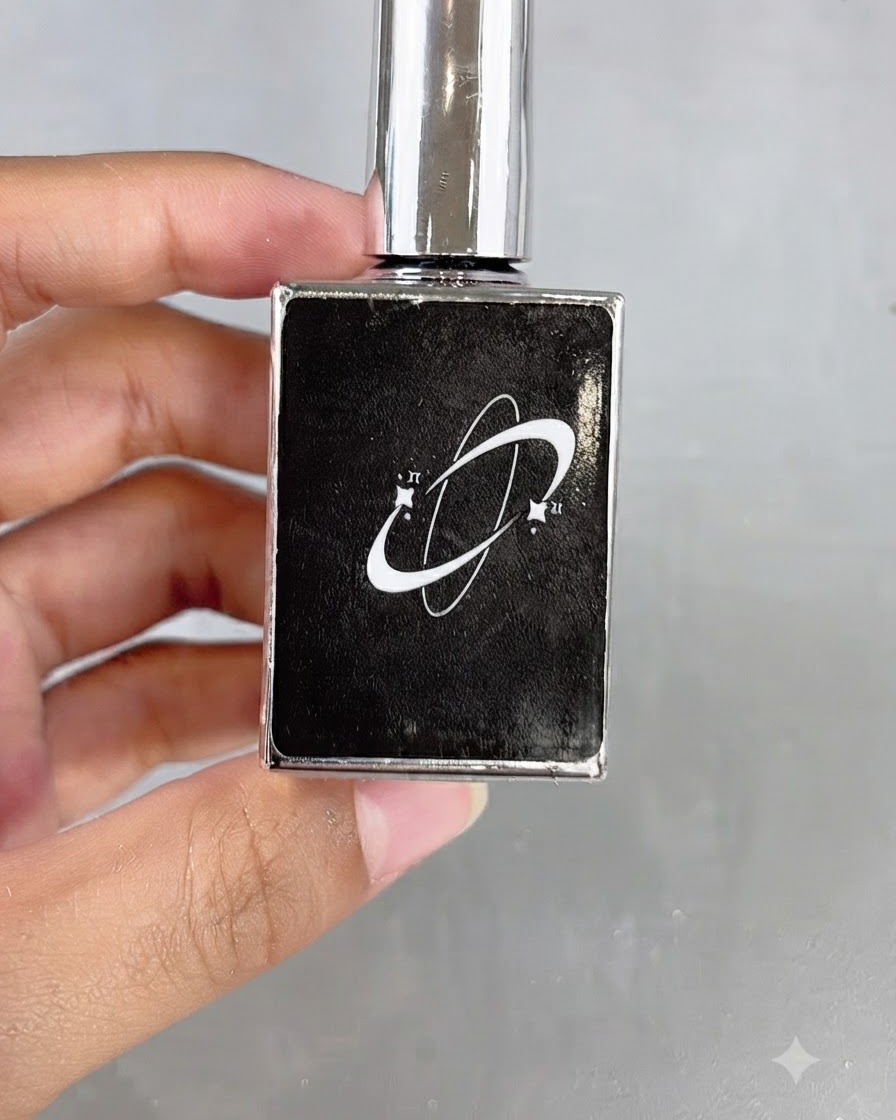 Un flacon de cosmétique noir arborant un logo en forme de planétoïde tenu en main.