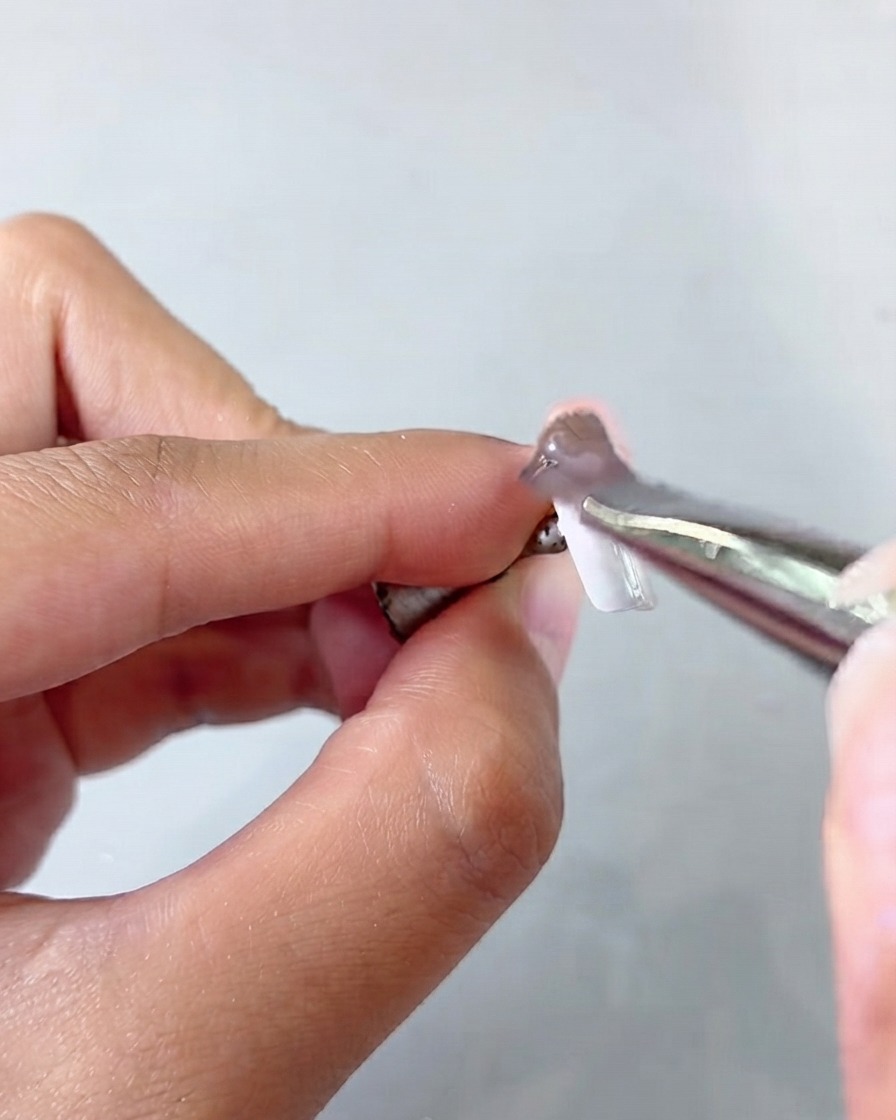 Une paire de pinces tenant une capsule dongle tout en appliquant une couche de gel cat eye.