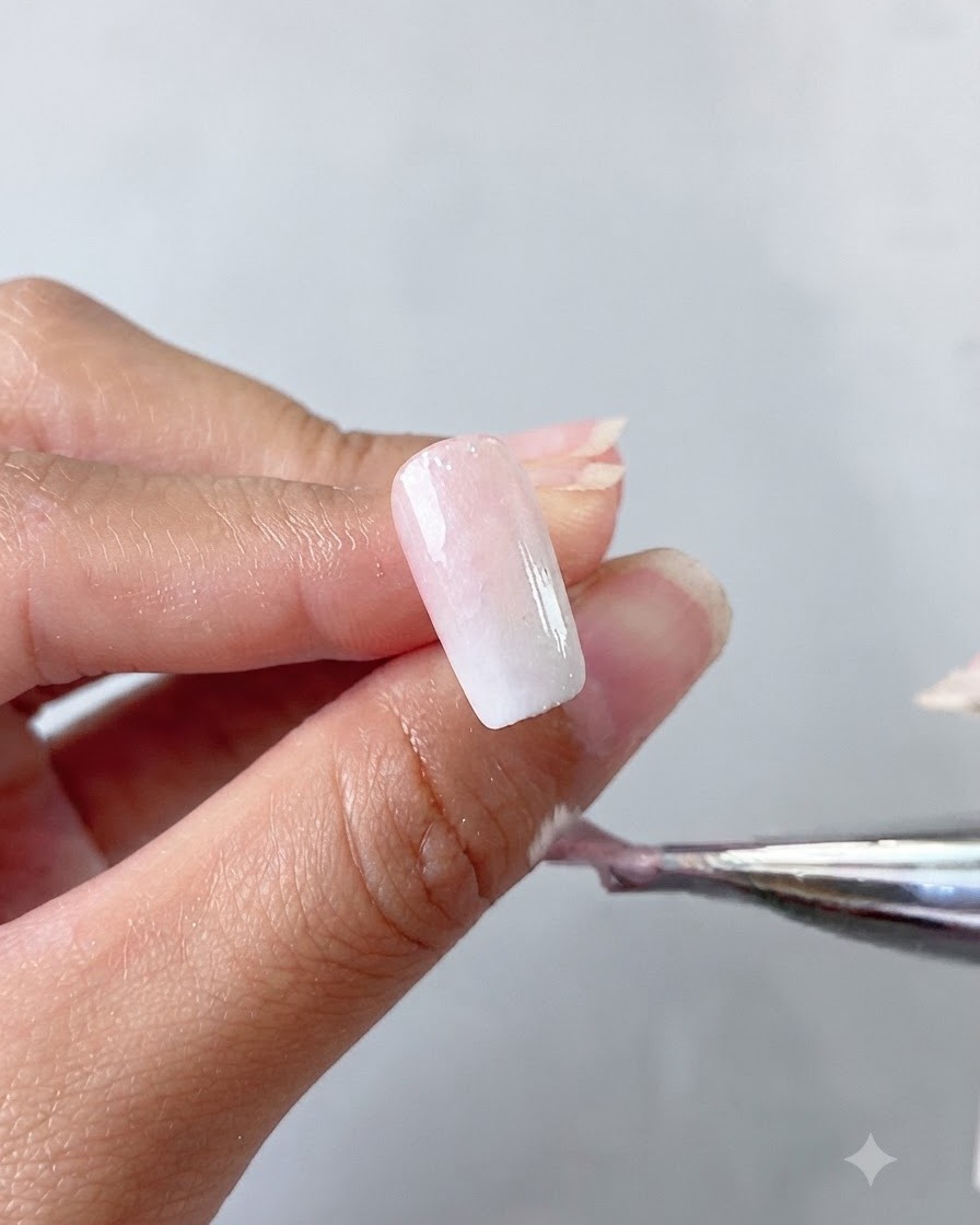 Une main tenant un pinceau appliquant une couche de base en gel cat eye blanc laiteux sur un ongle.