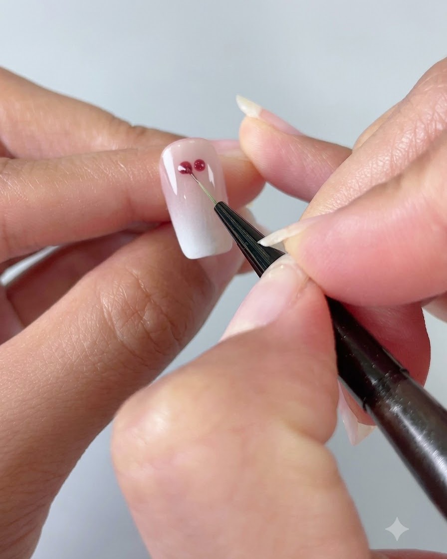 Un pinceau liner de nail art fin raccordant deux points de gel rouge en forme de cœur sur un ongle dégradé cat-eye.