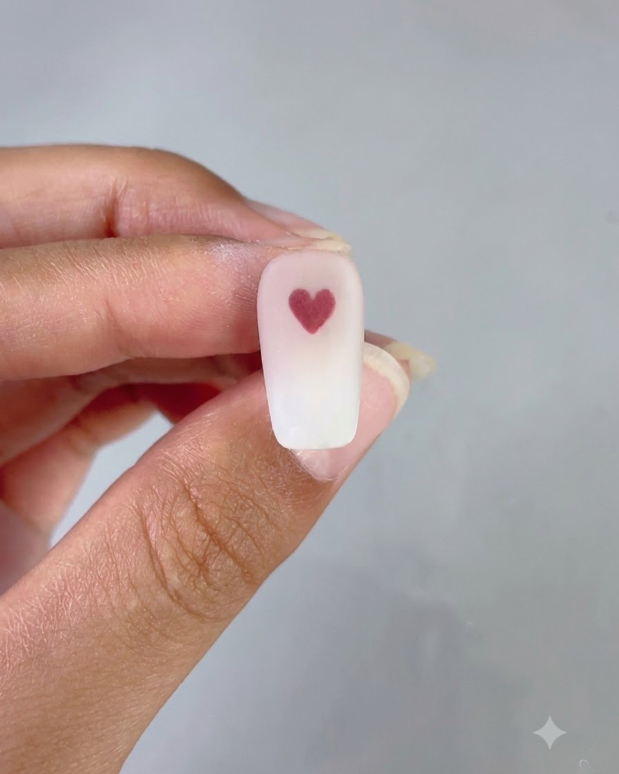 Un ongle fini arborant un dégradé rose et blanc soigné avec un cœur rouge net au centre.
