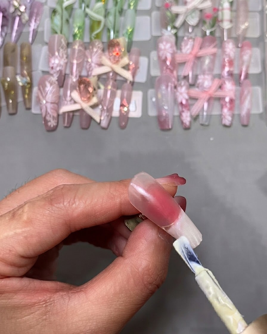 Un pinceau à vernis gel appliquant du vernis blanc sur le bout dun faux ongle fixé sur un support.