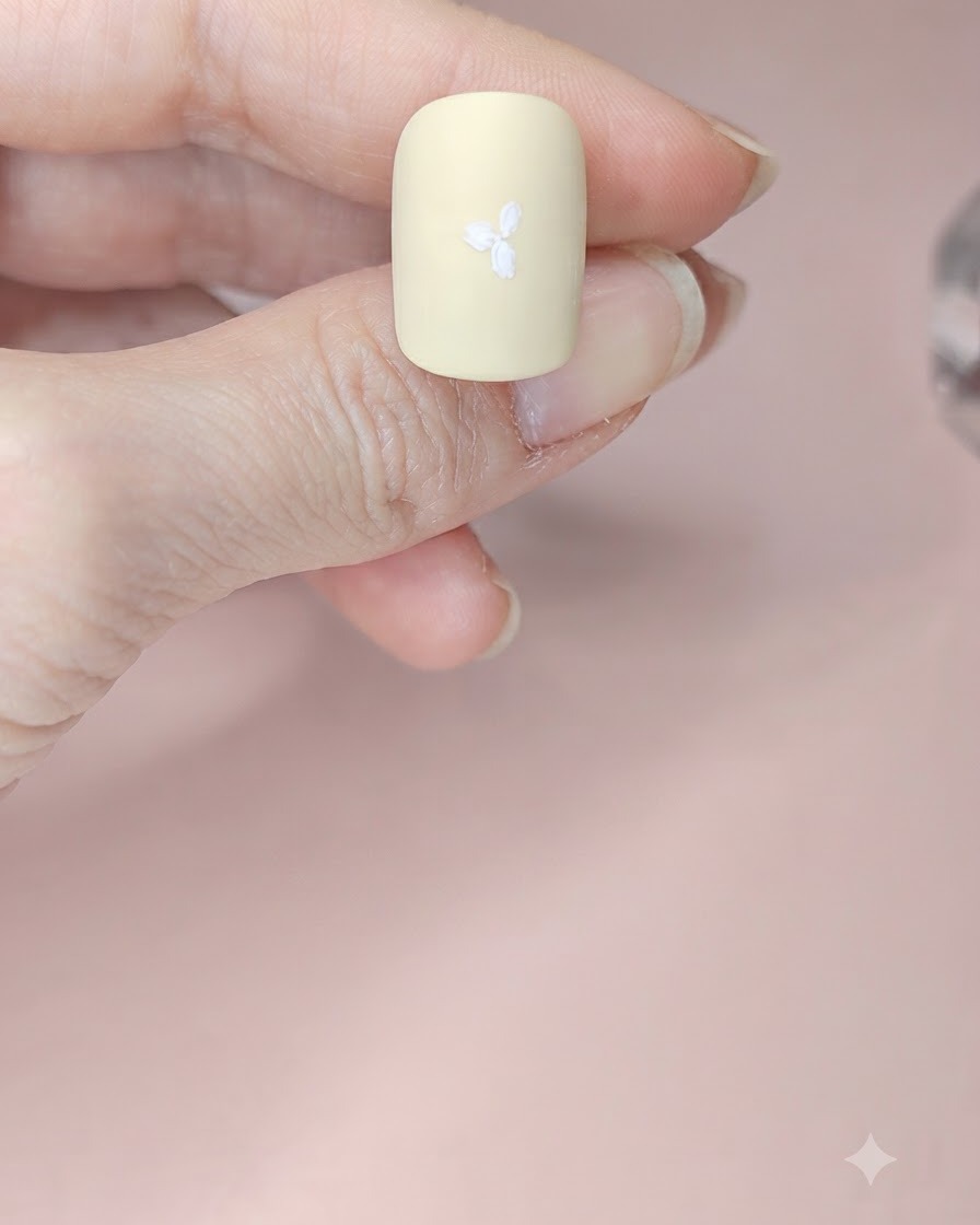 Un ongle jaune pâle avec trois fleurs blanches peintes sur toute la surface.