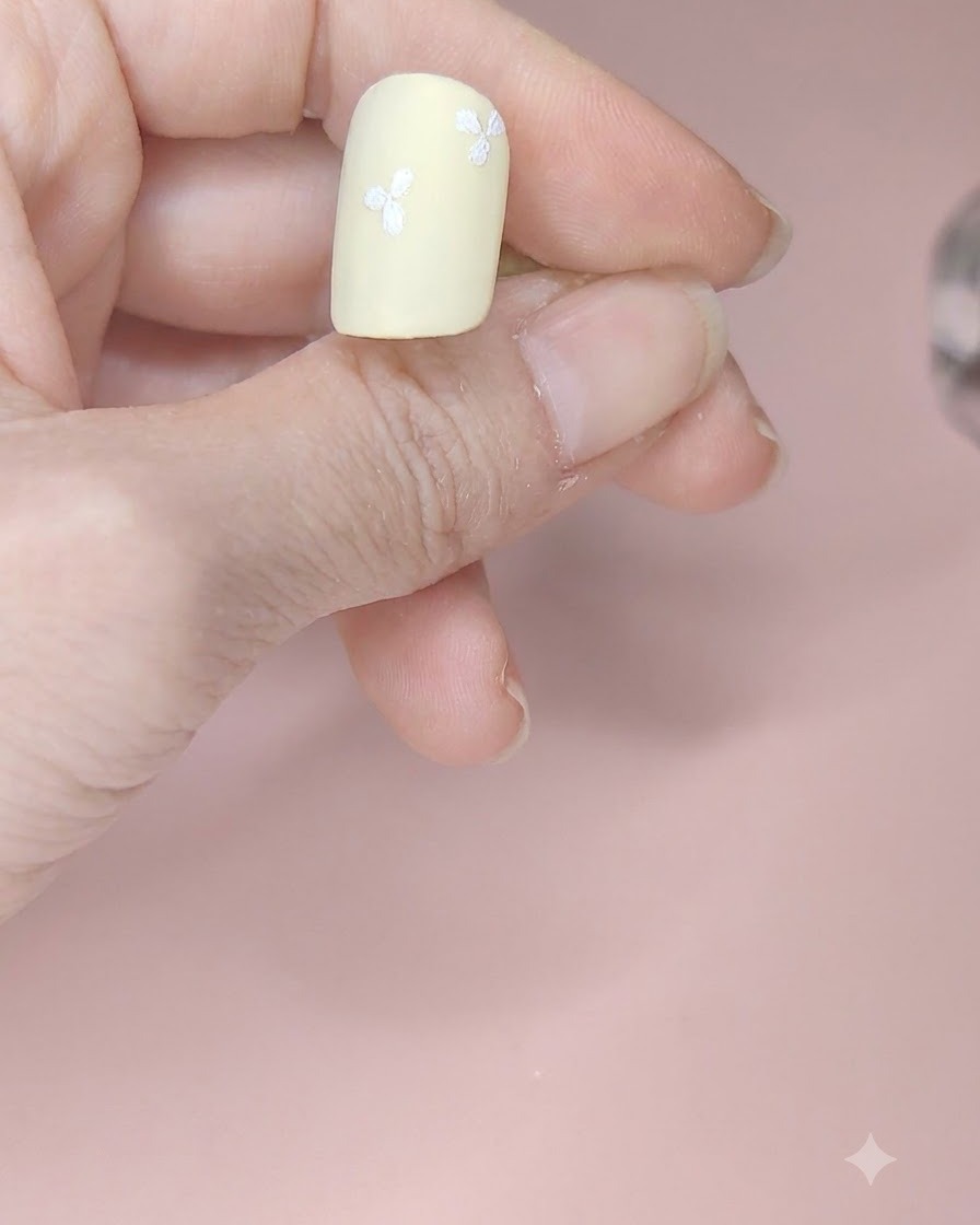 Un ongle jaune pâle présentant quatre fleurs blanches à trois pétales disposées sur différentes zones.