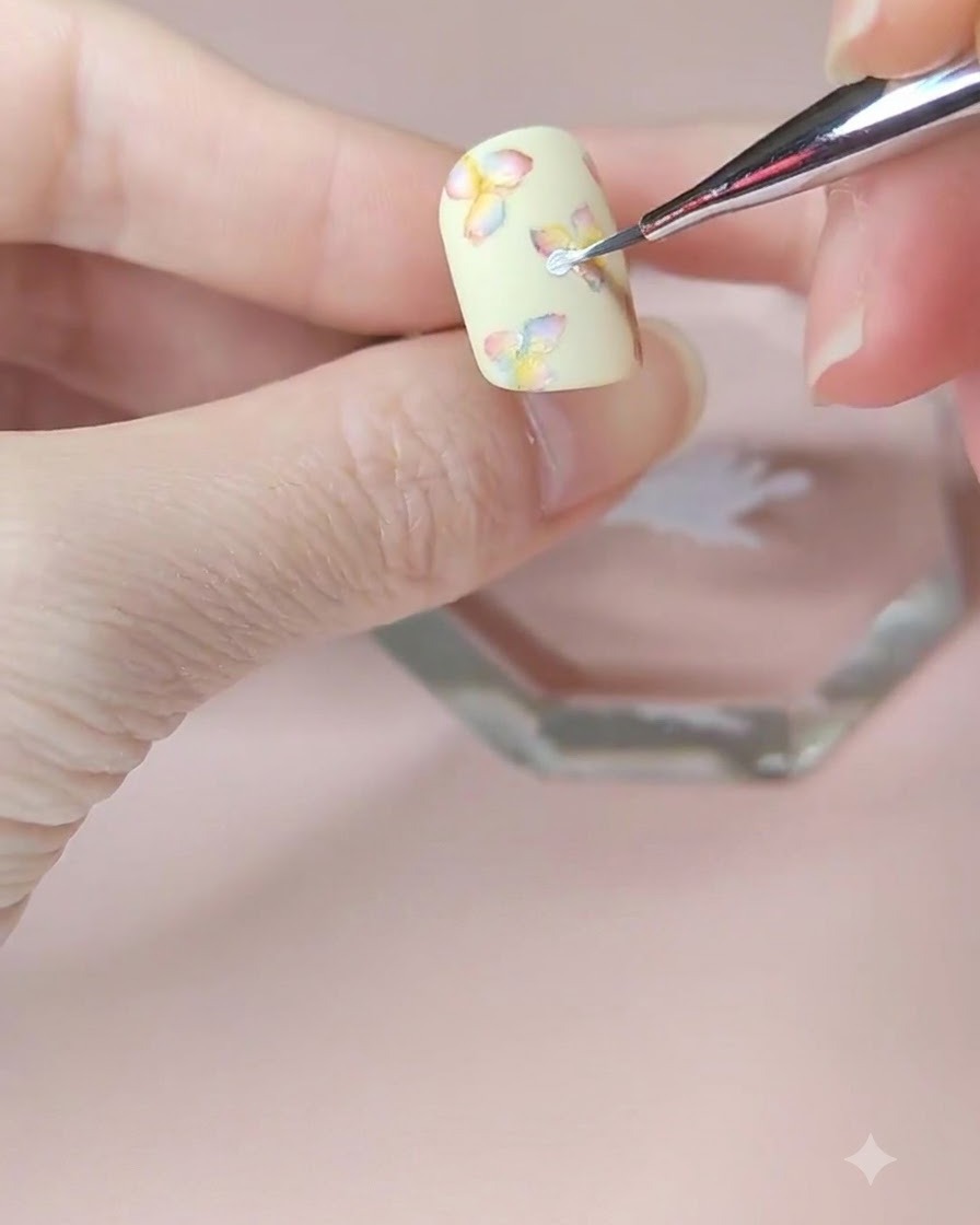 Un gros plan détaillé dun pinceau de nail art fin ajoutant une deuxième couche de pétales blancs à la fleur centrale.
