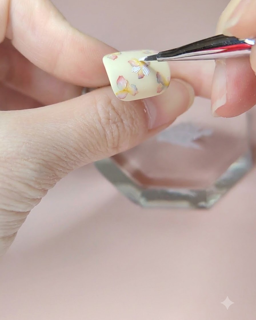 Un pinceau fin appliquant une deuxième couche de pétales blancs sur la fleur supérieure gauche de longle.