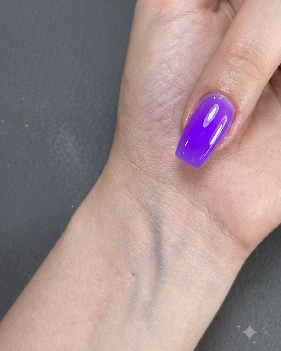 Une main avec un onglet vernis violet reposant près dune surface sous un éclairage.