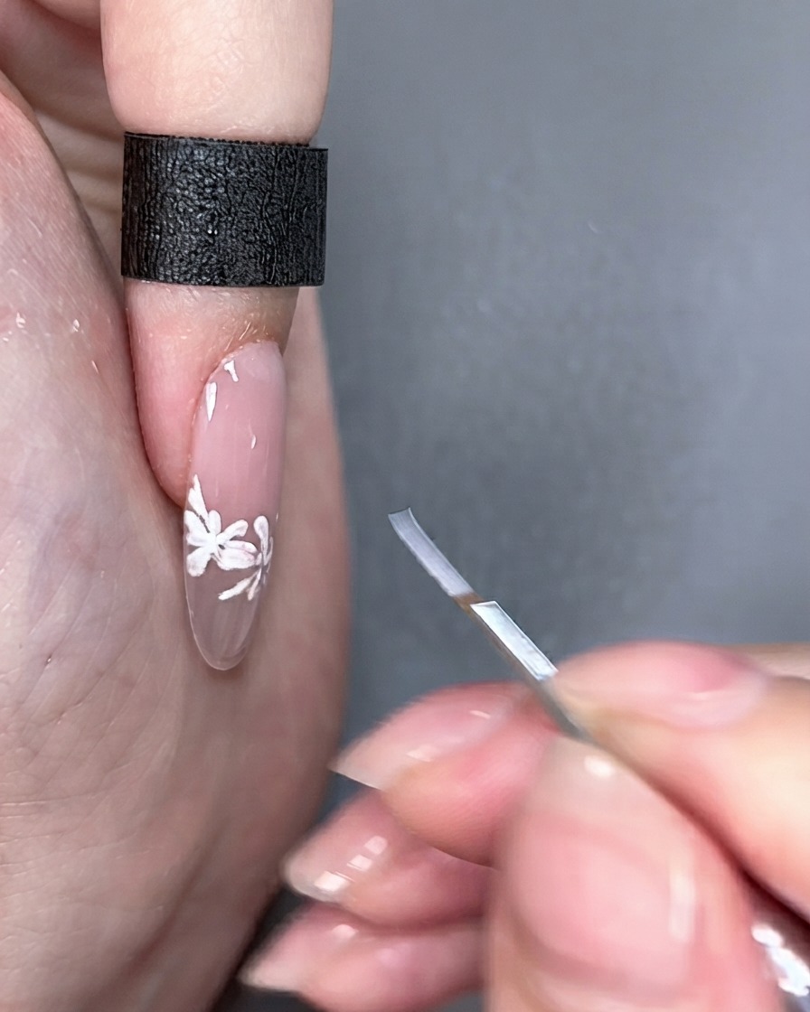 Un pinceau de nail art tenu à côté dun ongle fini sous un éclairage de studio.