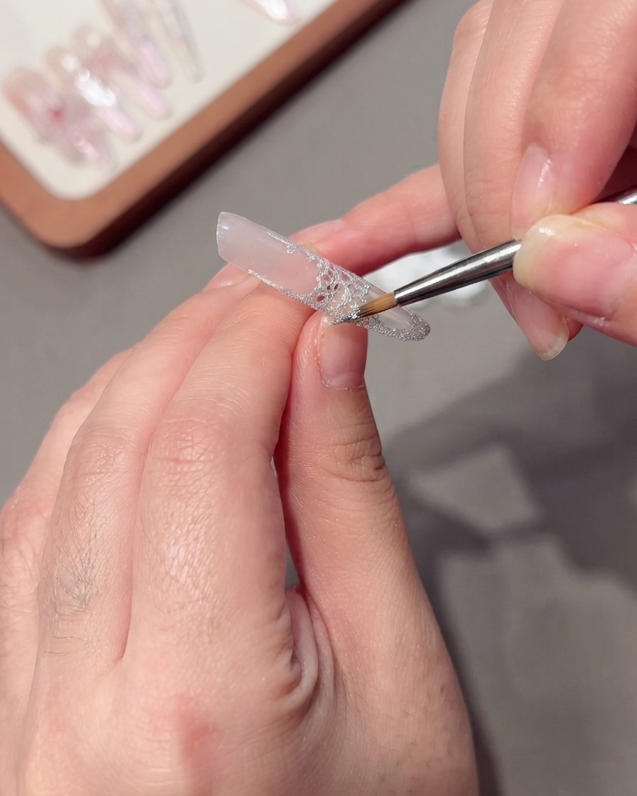 Un pinceau fin appliquant du gel étirable argenté pailleté le long du bord dun ongle en dentelle.