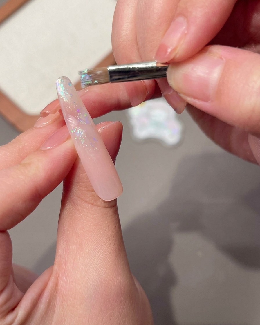 Un pinceau à ongles appliquant une couche fraîche de gel de base sur un ongle rose.