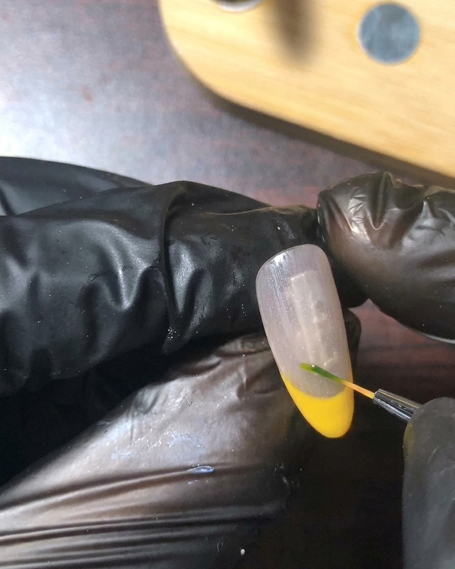 Un pinceau de détail fin peignant une minuscule tige verte et une feuille près de la ligne de sourire de longle.