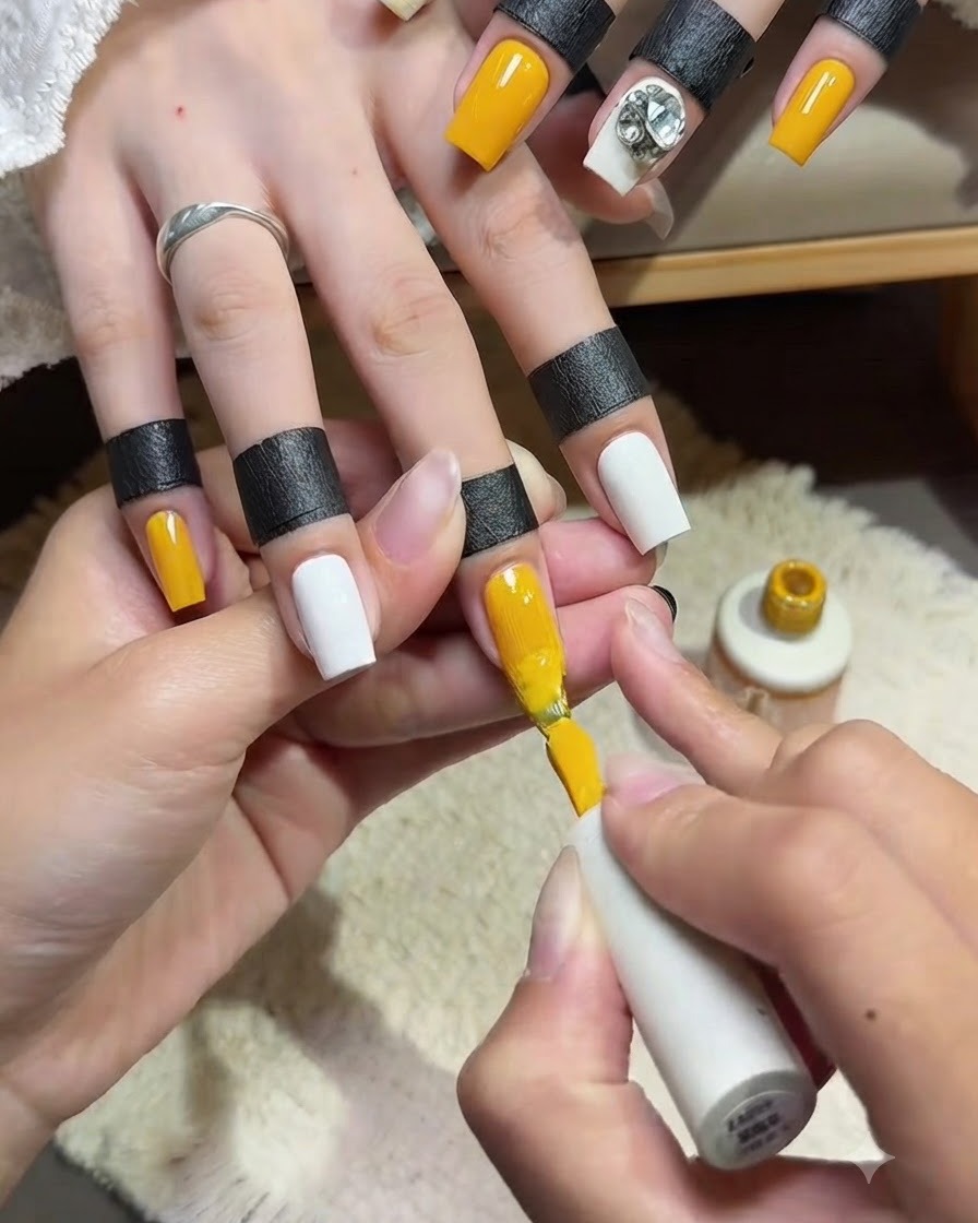 Gros plan dune prothésiste ongulaire appliquant une seconde couche lisse de vernis gel jaune vif sur longle dun index à laide du pinceau à vernis.