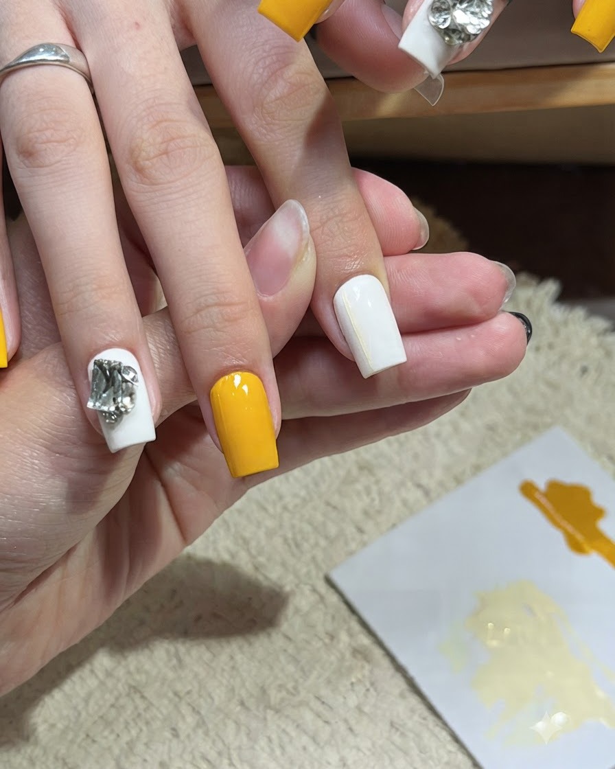 Un pinceau de nail art appliquant une deuxième fine ligne horizontale jaune sur un ongle blanc.