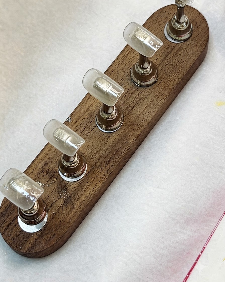 Un pinceau appliquant une base coat transparente sur des capsules dongles fixées sur un support en bois.