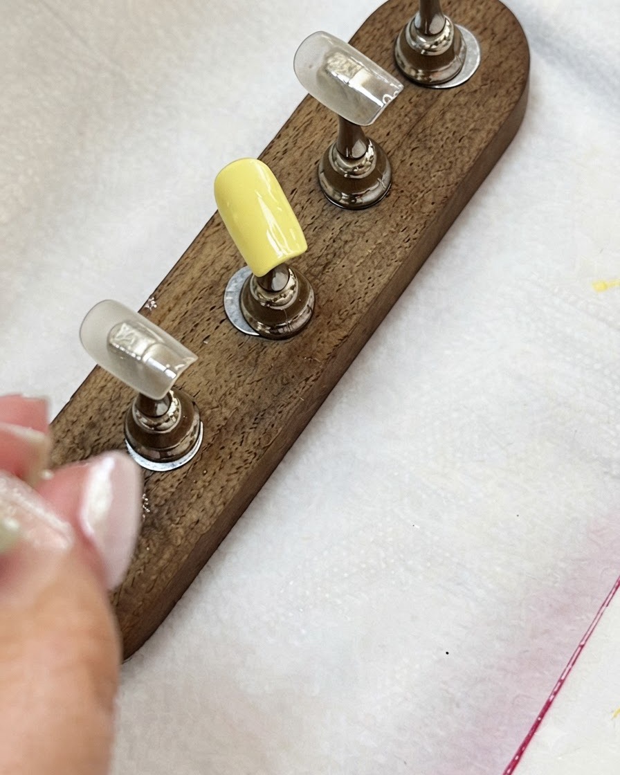 Capsules dongles sur un support en bois montrant une capsule jaune lacté et des capsules de couleur nude.