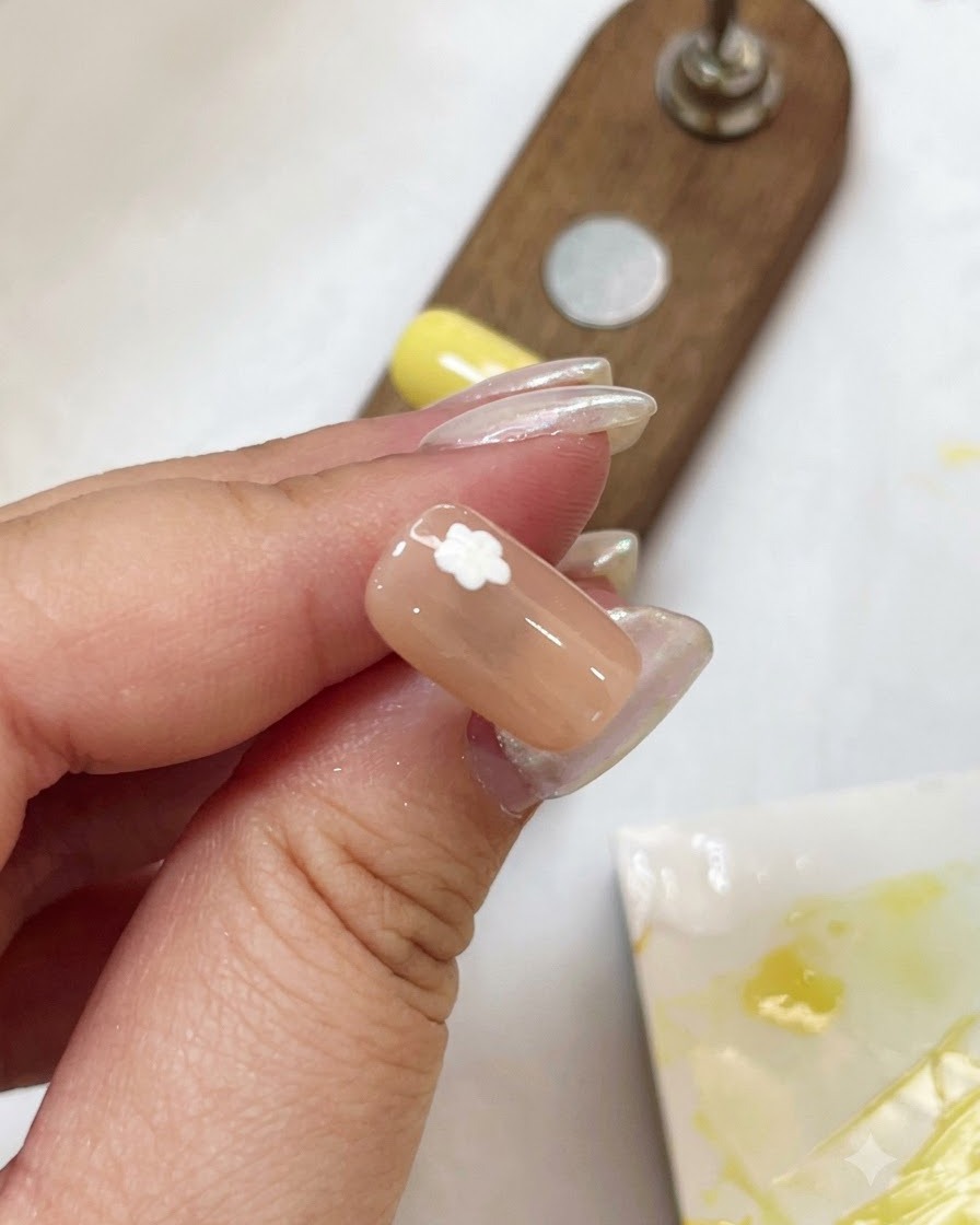 Gros plan dun ongle nude avec un motif de pétale de fleur blanc catalysé à laide dune petite lampe stylo UV violette.