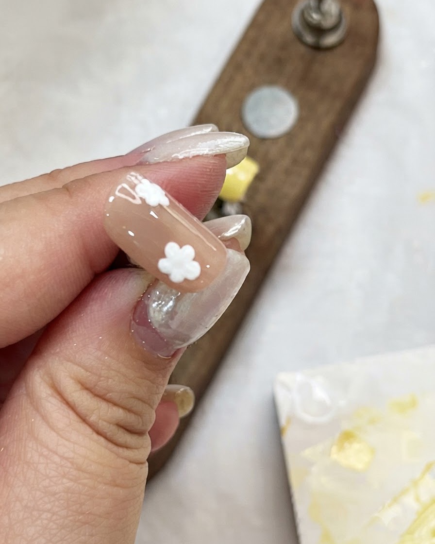 Une main tenant une capsule couleur nude tout en ajoutant des points blancs pour créer des fleurs.