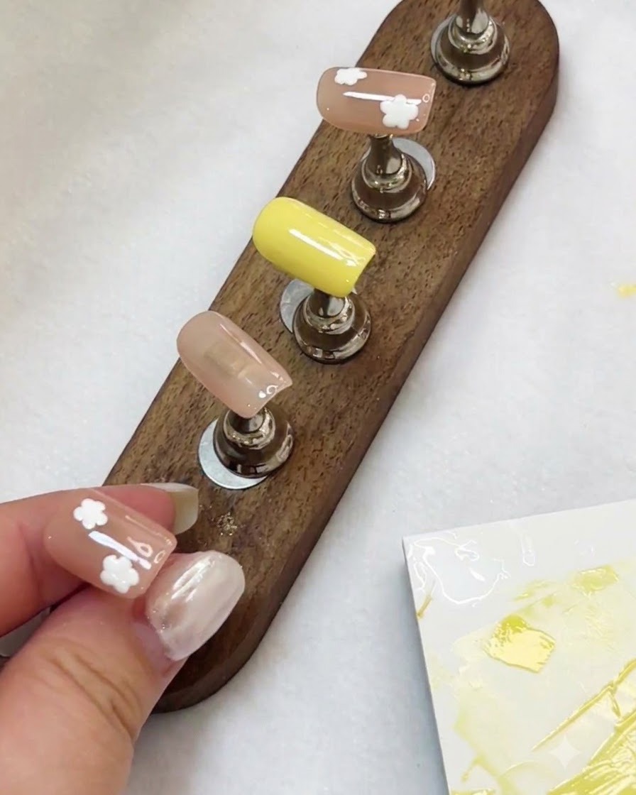 Un présentoir contenant plusieurs faux ongles peints avec des motifs de fleurs blanches sous la lumière.