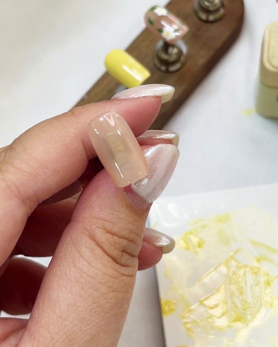 Gros plan dune main tenant une capsule couleur nude pendant lapplication dun gel cat-eye scintillant avec un pinceau.