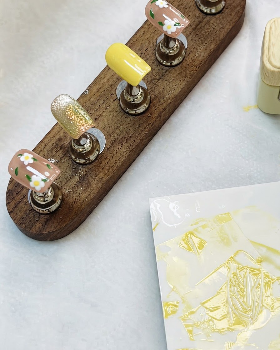 Un présentoir en bois contenant des capsules de nail art floral et cat-eye terminées sur une table.