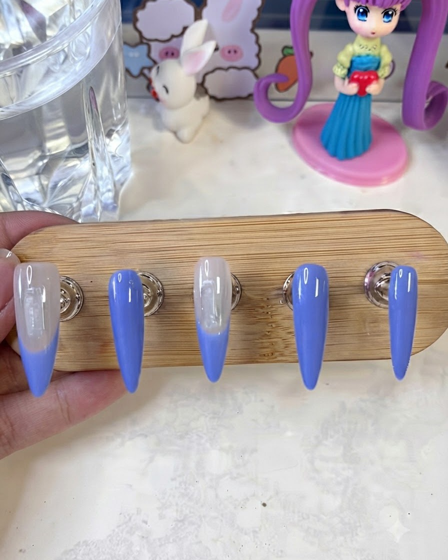 Un pinceau de nail art appliquant une deuxième couche de peinture de french bleue sur le bord des ongles sur un support de présentation.