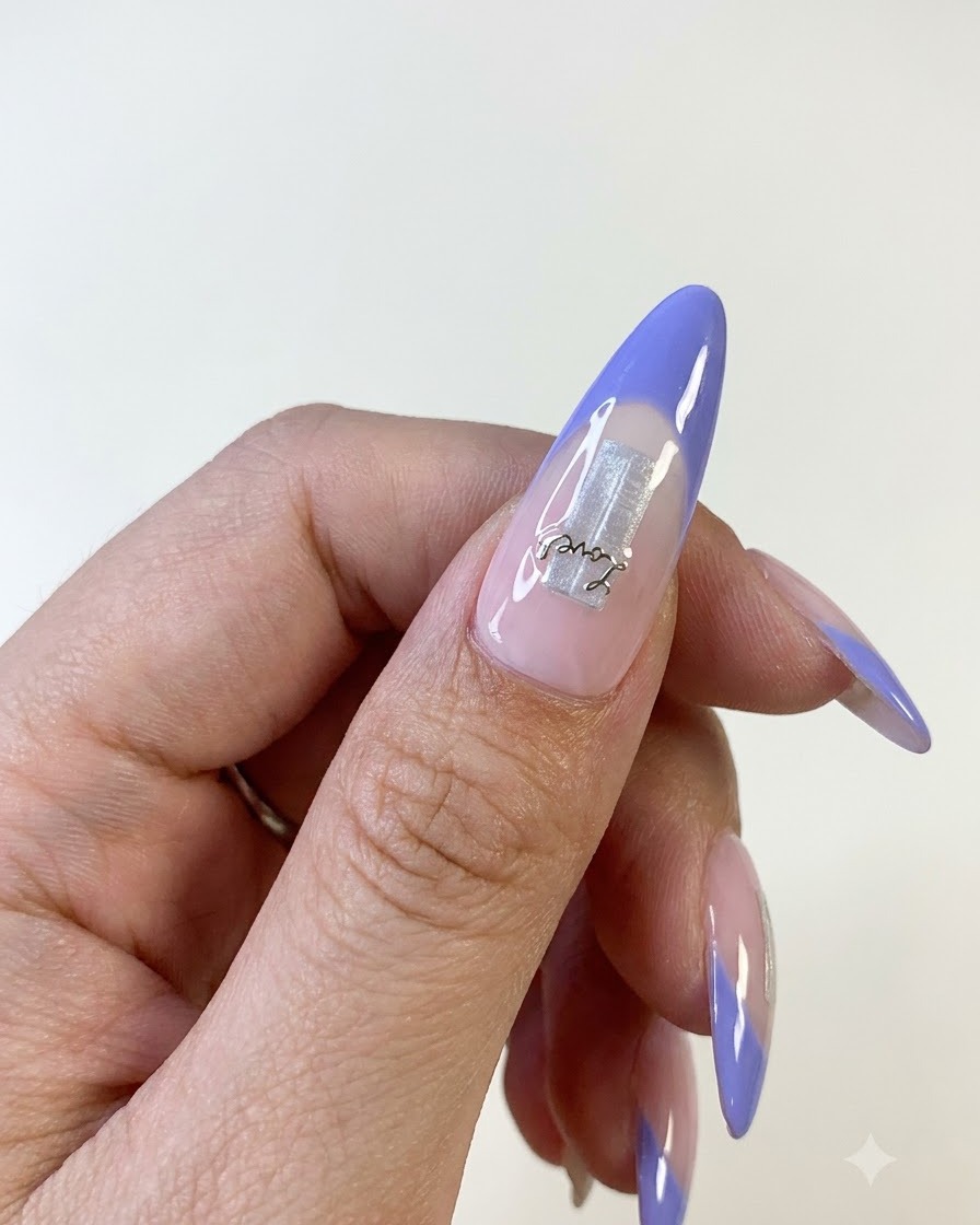 Gros plan dun ongle de pouce comportant une french bleue, un élément de base en feuille argentée et un délicat sticker de lettre.