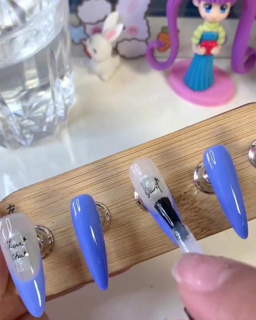 Un pinceau à ongles appliquant une couche transparente de gel de renforcement sur la surface dun ongle avec des stickers de lettres.