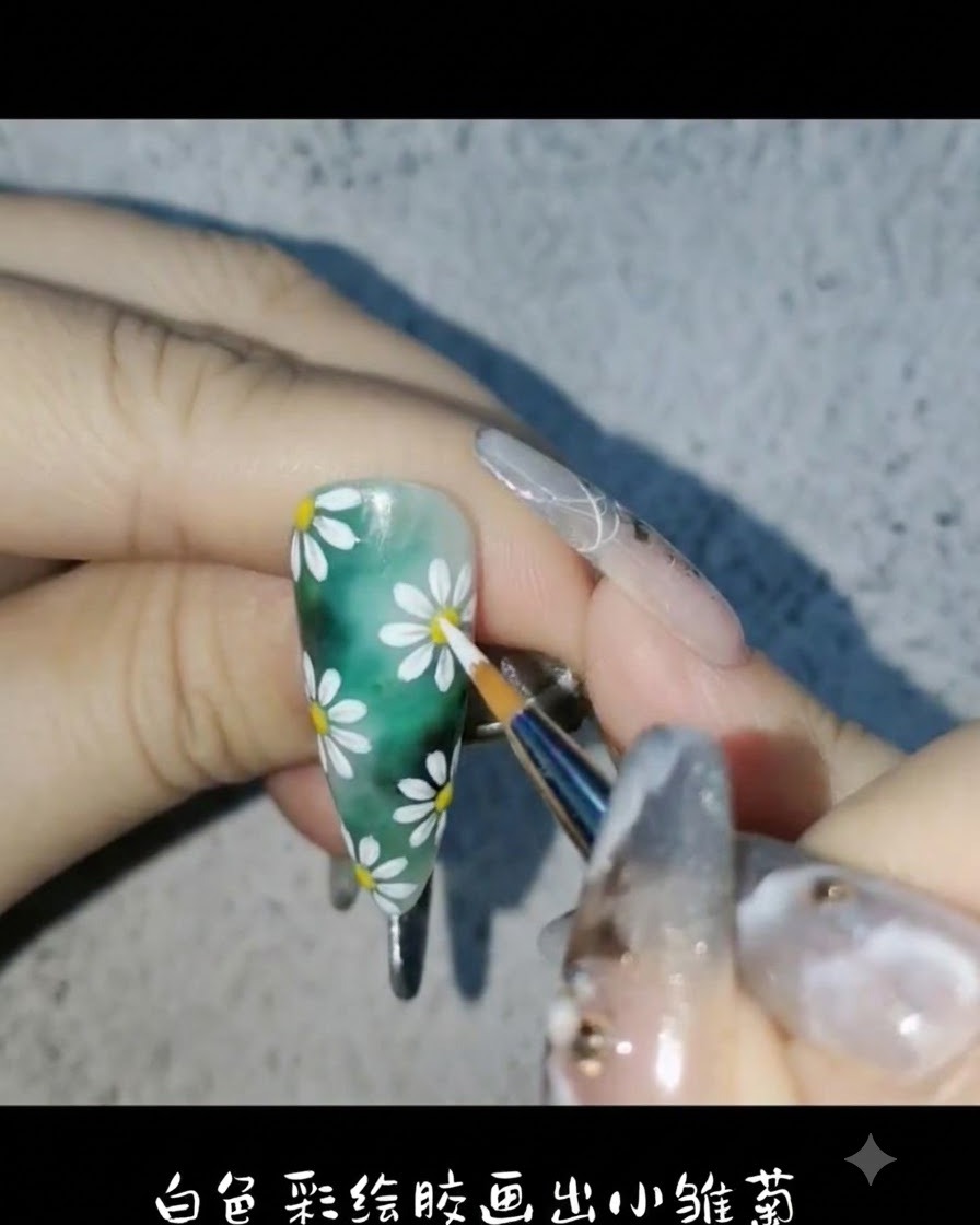 Un pinceau liner utilisant du gel de peinture blanc pour dessiner de délicats pétales de marguerite sur le fond dongle vert.