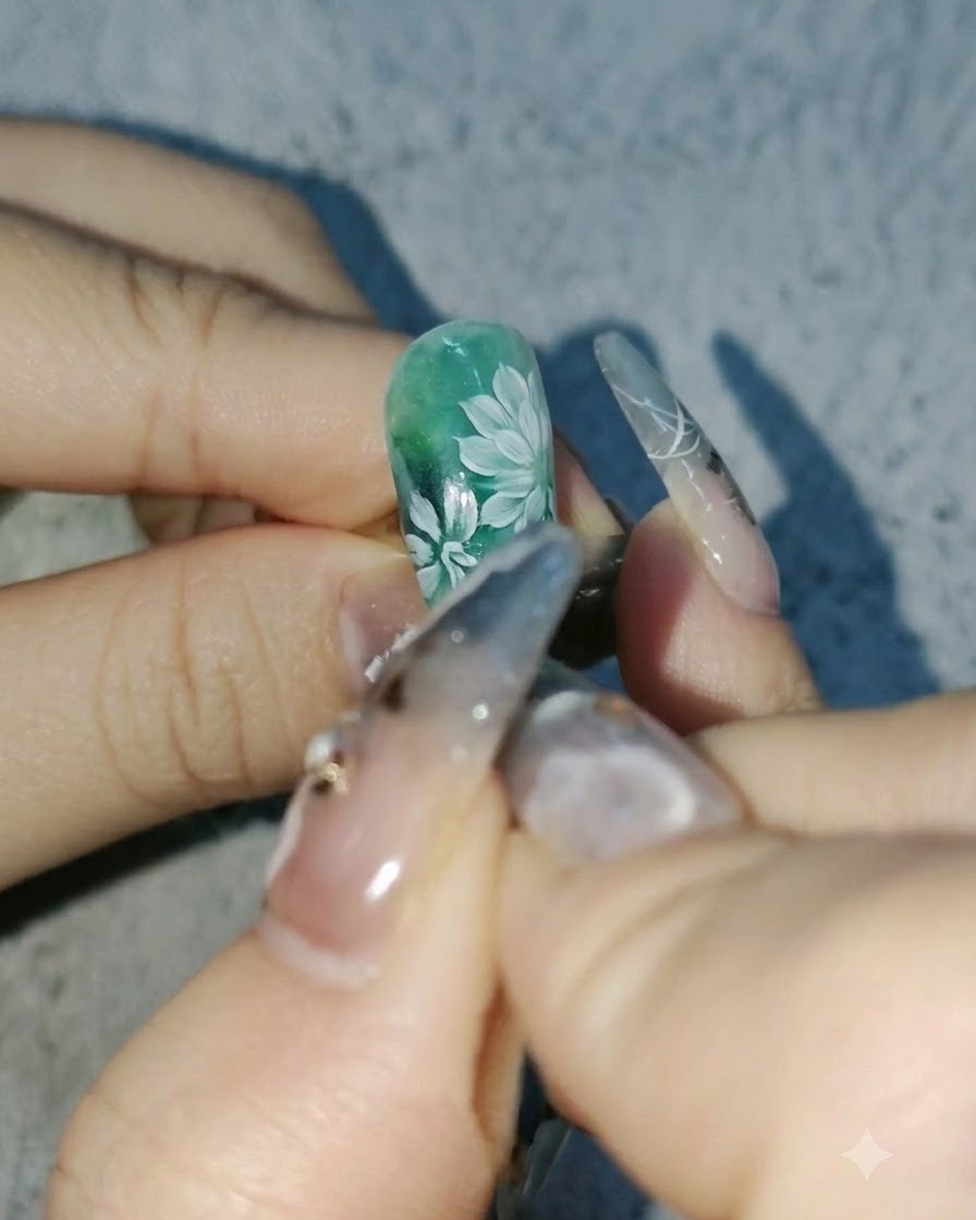 Vue rapprochée dune prothésiste ongulaire ajoutant des pétales blancs plus profonds aux marguerites sur un design dongle vert.