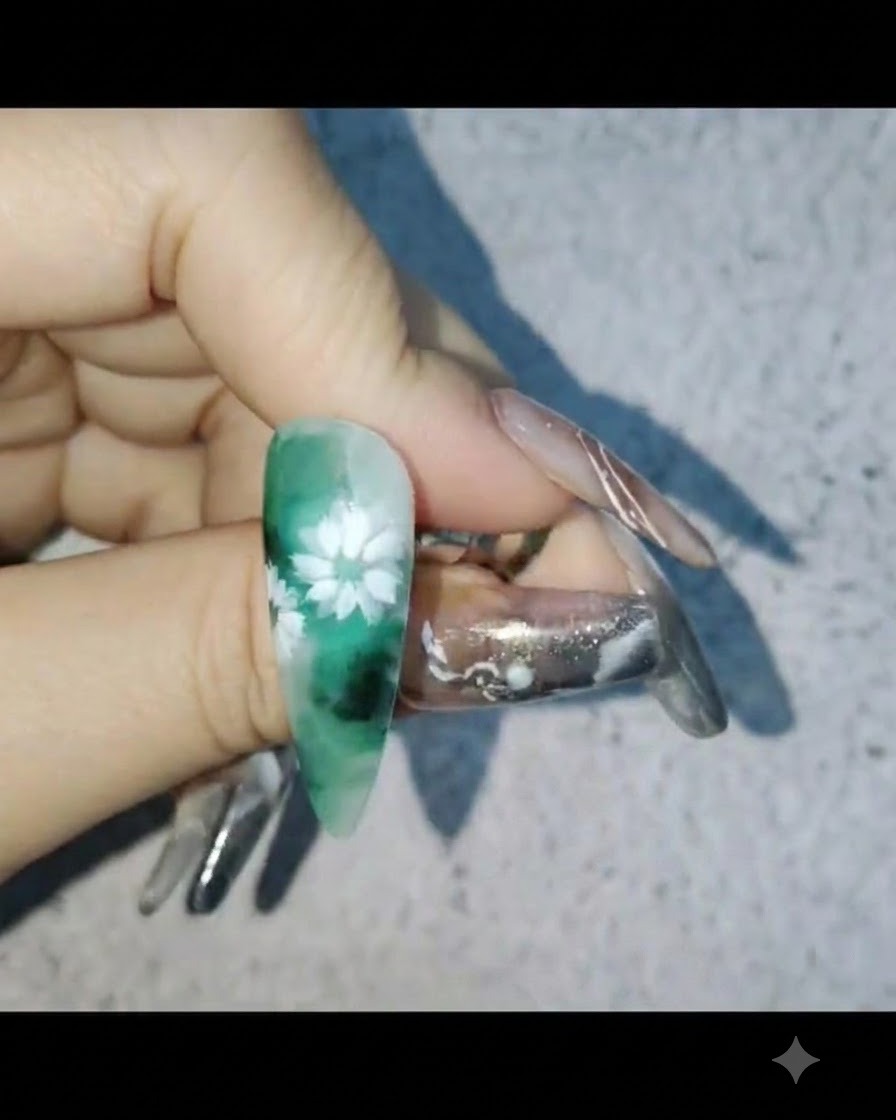 Une main tenant un ongle avec un nail art marguerite blanche tout en appliquant une couche protectrice de gel de renforcement.