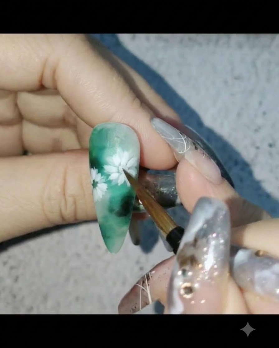Un pinceau à ongles appliquant un top coat mat sur un design dongle floral à thème vert.