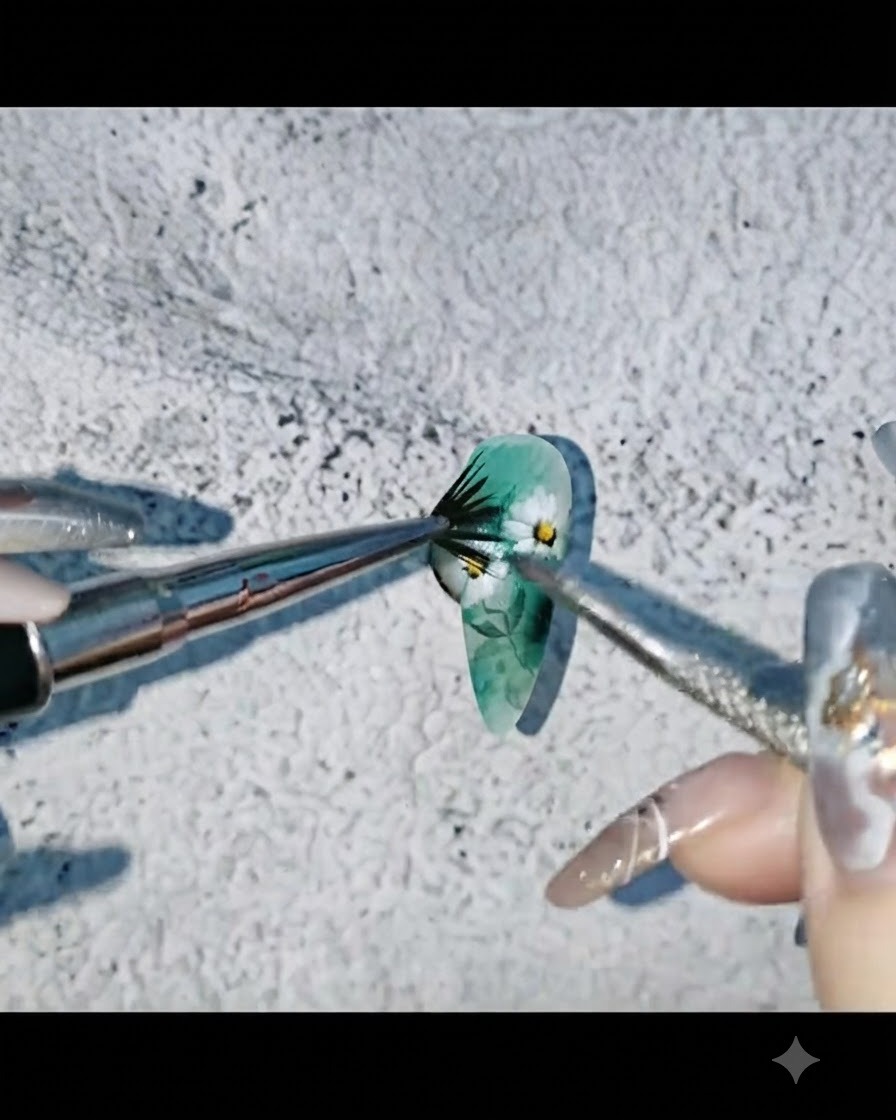 Une prothésiste ongulaire projetant de la peinture aquarelle noire sur un bout dongle vert et floral décoré.