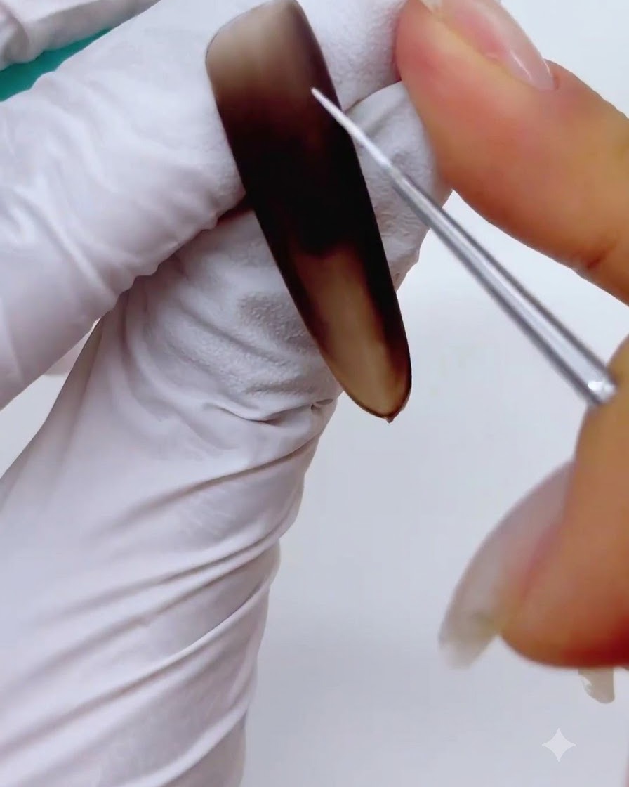 Gros plan dun pinceau liner fin pour nail art peignant de fines lignes blanches entrecoupées pour former un squelette de flocon sur un ongle brun mat.