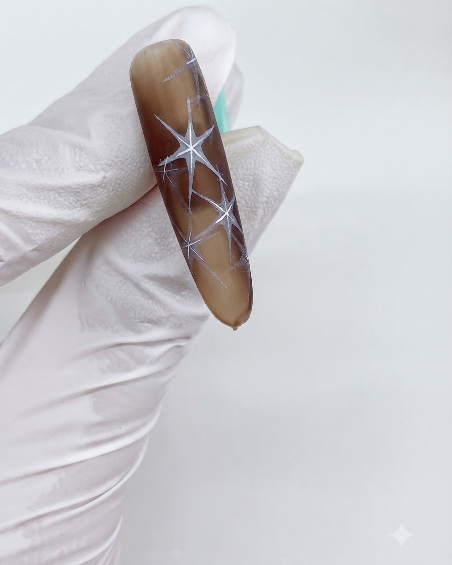 Gros plan dun ongle en dégradé brun avec des motifs détoiles blanches complexes en cours de catalysation.