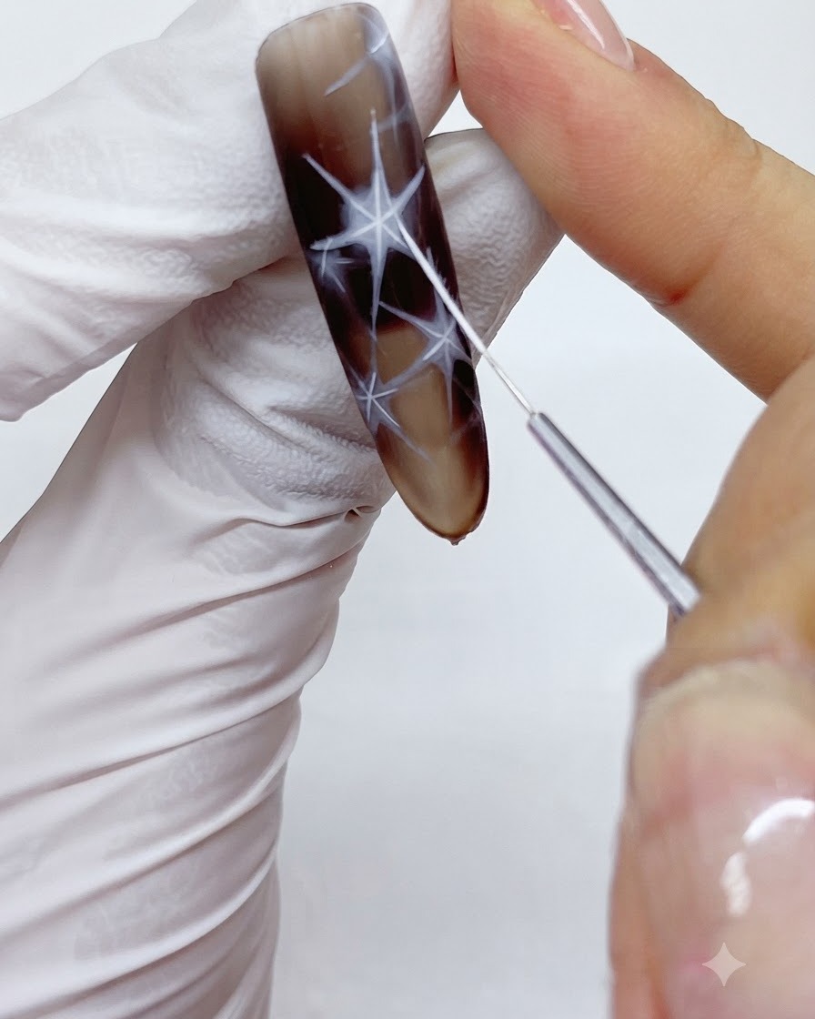 Un pinceau liner fin traçant et contournant soigneusement les bordures extérieures dun motif détoile blanche sur un ongle.