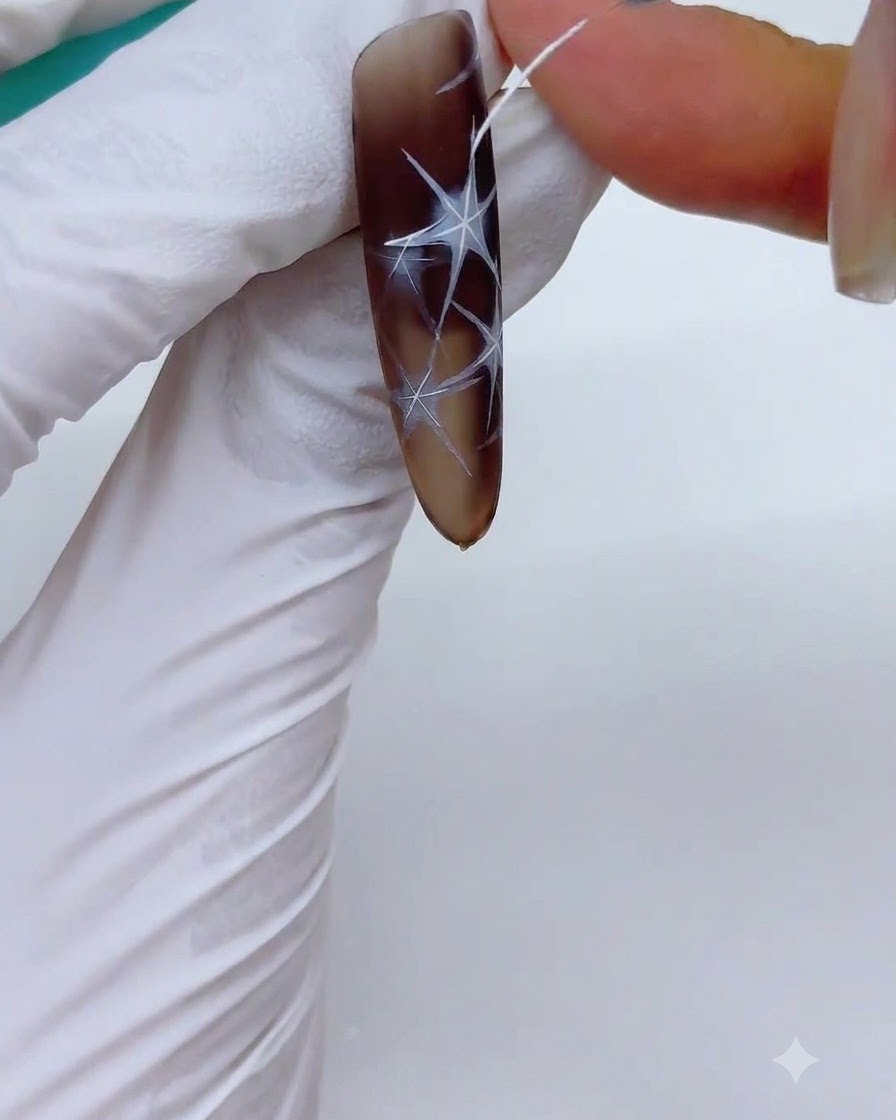 Un ongle avec des motifs détoiles blanches contournés placé dans une lampe UV/LED pour catalysation.