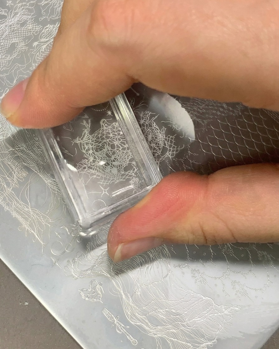 Un tampon transparent transférant un motif de dentelle blanche sur une capsule dongle transparente.