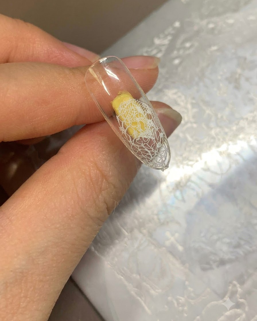 Une capsule dongle transparente montrant un motif de dentelle blanche transféré à lextrémité et une base gel beige appliquée sur le reste.