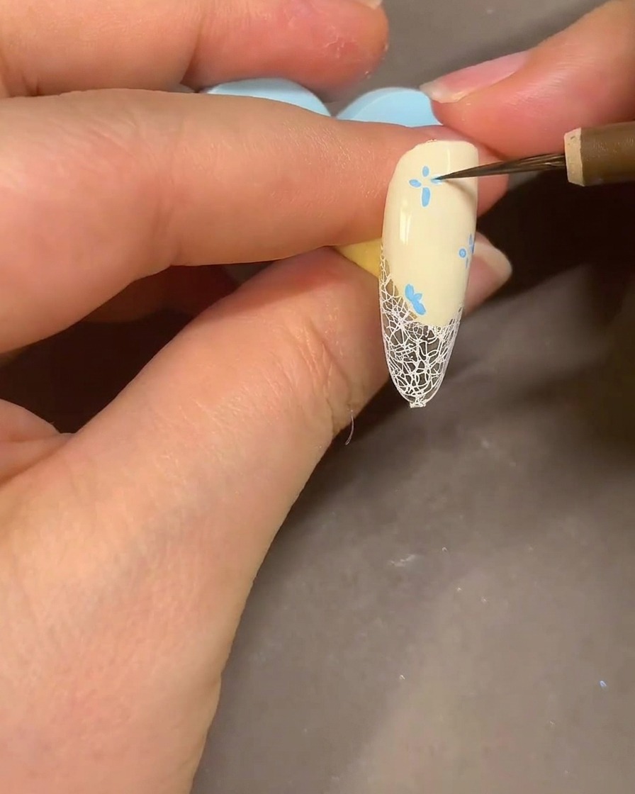 Un pinceau aquarelle estompant les pétales de fleurs au feutre bleu sur un ongle avec de lalcool pour un effet fumé.