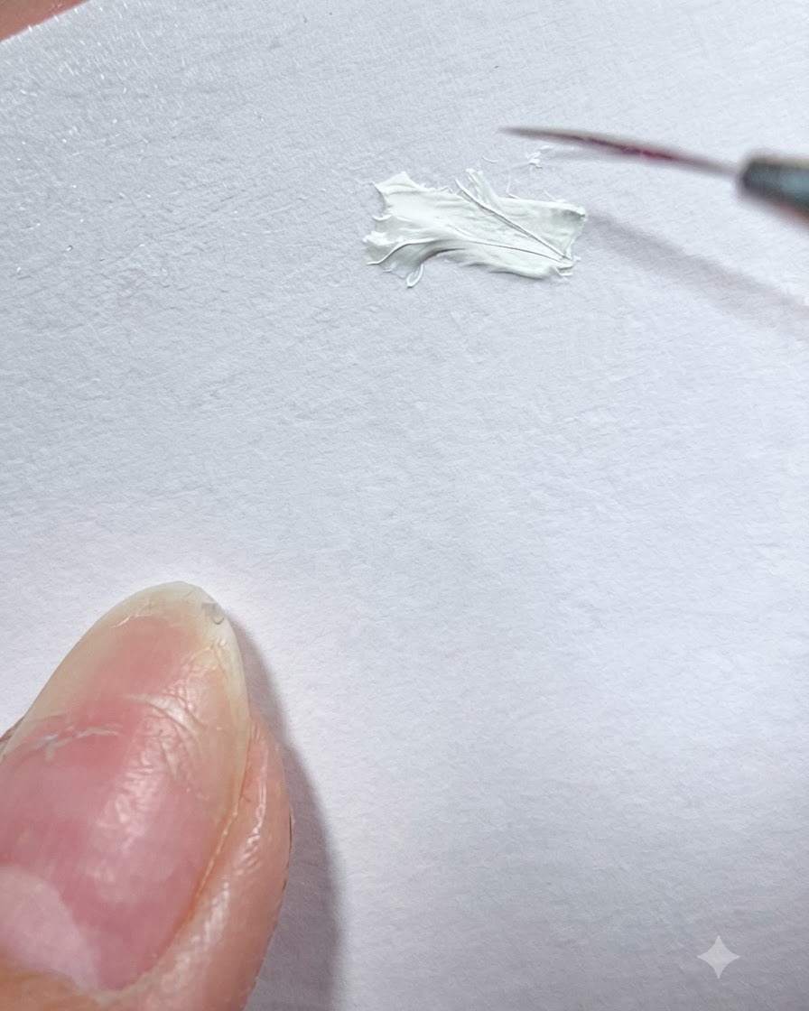 Un pinceau fin de détail prélève du gel peinture blanc sur une palette de surface blanche.