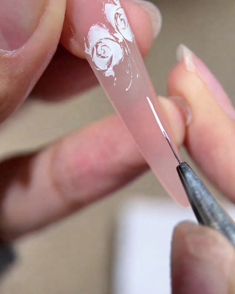 Une vue rapprochée dune prothésiste ongulaire dessinant une forme de parenthèse blanche sur une plaque dongle rose.