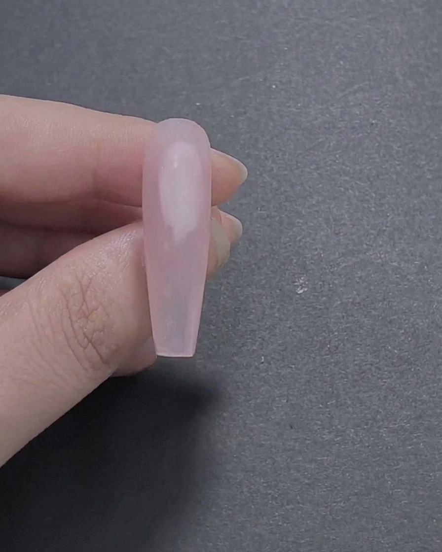 Un gros plan d un ongle long en forme de cercueil peint avec une couche de base en gel rose diaphane lisse et brillante tenue entre des doigts.