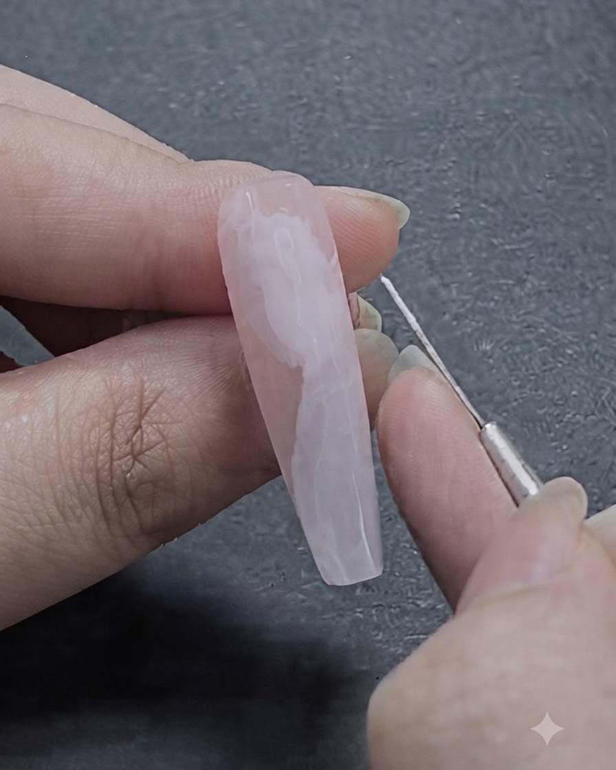 Un pinceau liner fin pour nail art dessinant des lignes blanches délicates sur le design de ruban en blooming gel semi-fondu.