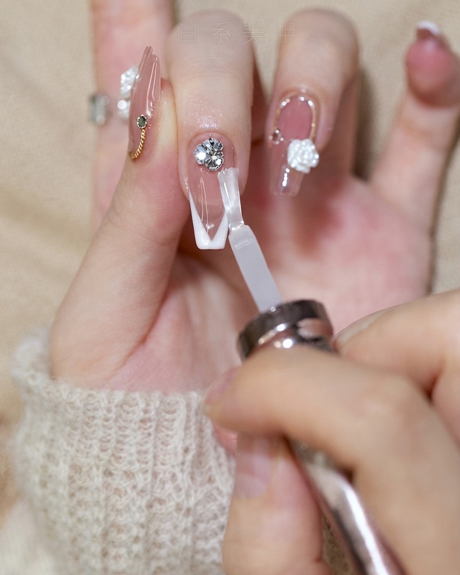 Un pinceau à ongles appliquant un top coat brillant sur un ongle en french tout en évitant le groupe de strass.