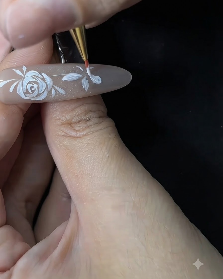 Une prothésiste ongulaire utilisant un pinceau fin pour affiner et épaissir les pétales blancs dune petite fleur sur une extension en gel.